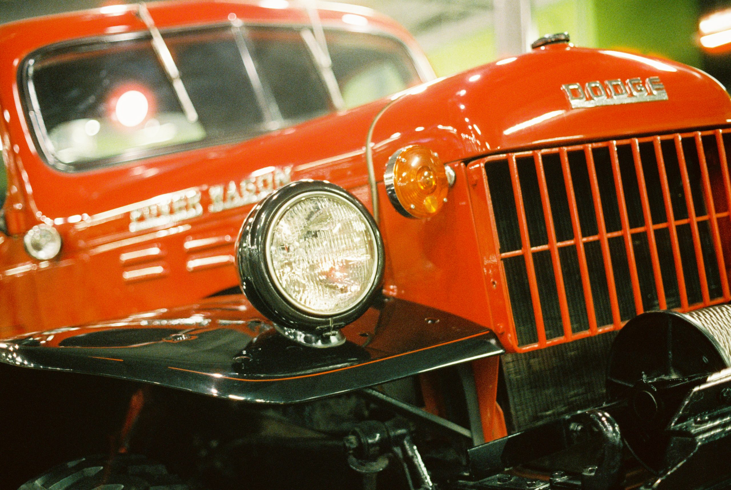 Close-up of a vintage red Dodge truck, focusing on the headlight and front grille. The image shows the vehicle's rugged design, with "Dodge" clearly visible on the front. The background is slightly blurred, highlighting the truck's bold and classic features—a timeless tribute to craftsmanship by Millworks Web Design & Graphics.