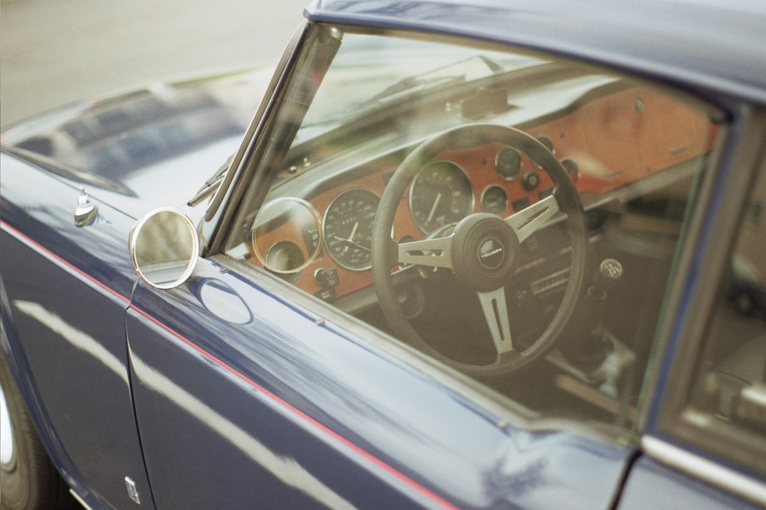 Close-up of a vintage car's interior, featuring the steering wheel, dashboard, and speedometer. The car boasts a wooden dashboard and classic design. Reflections on the window slightly obscure the view, reminiscent of the attention to detail one might find in Millworks Web Design & Graphics work.