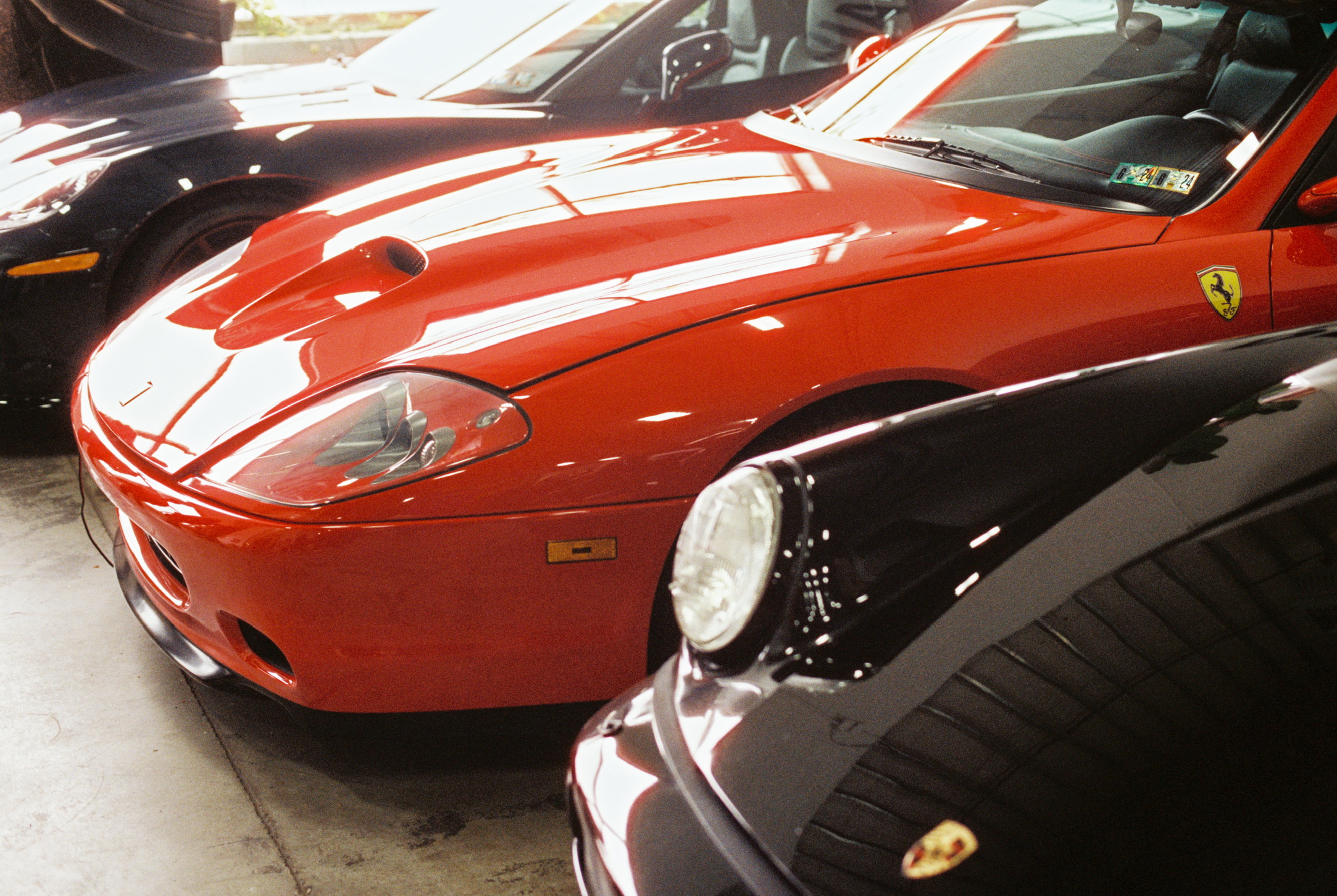 A red Ferrari is parked inside a garage, flanked by a black Porsche on the right and another dark-colored car on the left. The cars are closely aligned, highlighting their sleek and polished exteriors—a visual testament to precision akin to Millworks Web Design & Graphics’ custom websites.