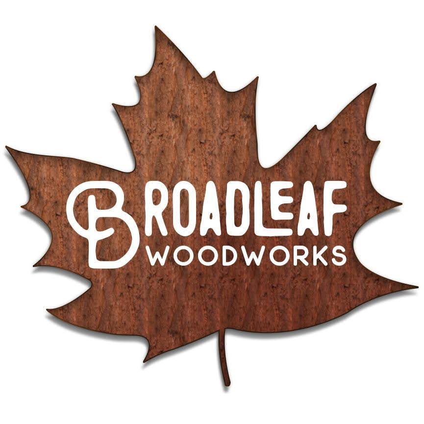 Logo for Broadleaf Woodworks. The logo features the company name in white, stylized text imposed on a textured, brown maple leaf shape with a cut-out design. Inspired by Millworks Web Design & Graphics, it embodies classic craftsmanship and refined graphic design.