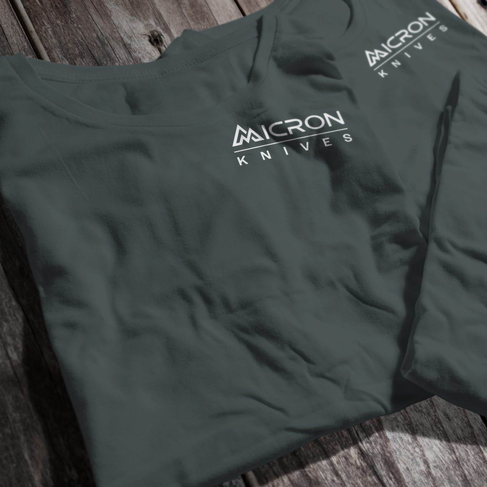 Folded dark gray Micron Knives T-shirts, featuring the white Micron Knives logo on the chest, arranged neatly on a rustic wooden surface.