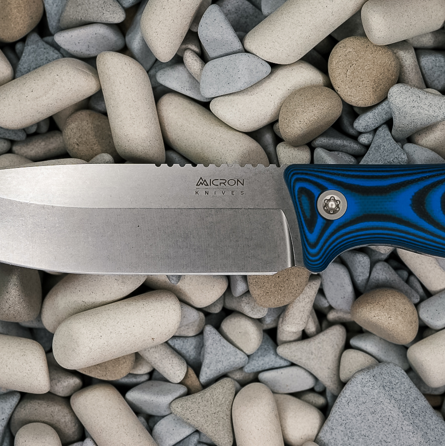 A close-up of a Micron Knives fixed-blade knife with a blue and black handle, resting on smooth, assorted grey and beige pebbles showcases the fine craftsmanship of Micron Knives.